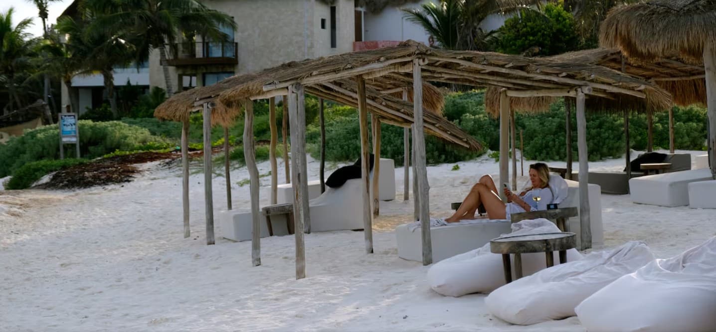 Palapas vacías con pocas personas en playa de arena blanca frente a hotel en Tulum.