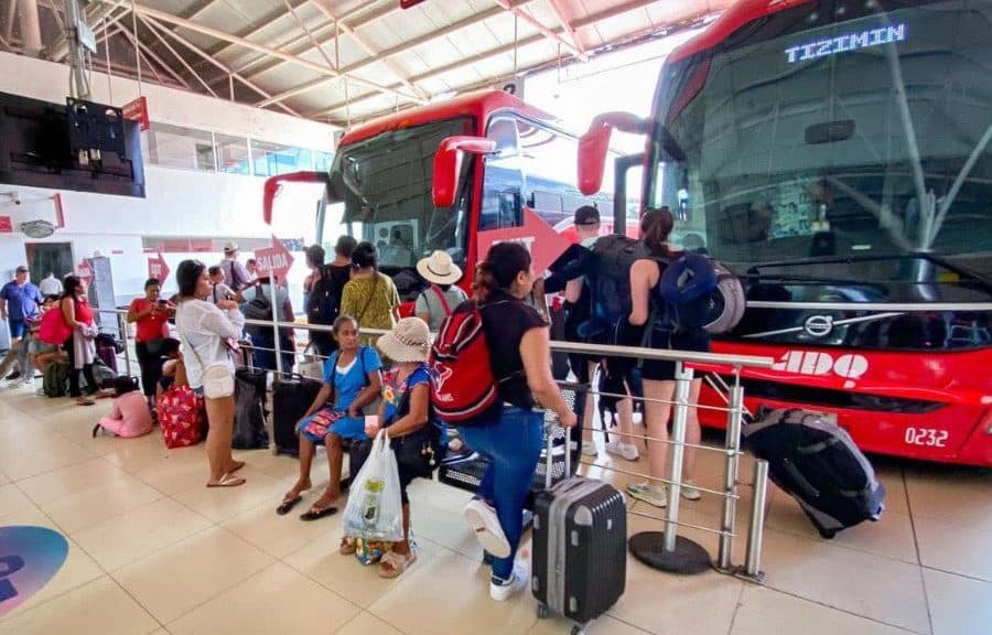 Pasajeros hacen fila para abordar autobuses rojos de la empresa Ado en una terminal de transporte foráneo.