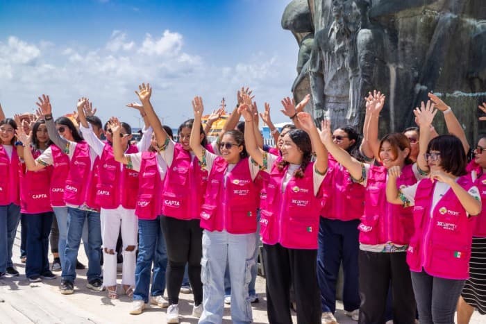 Grupo de personas en uniforme rosa con distintivos CAPTA levantando las manos frente a una estatua, en un acto de entrega de equipamiento.