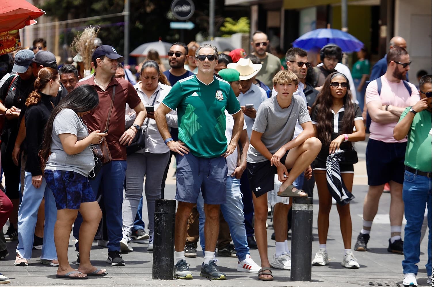 Grupo de turistas y personas en una calle peatonal soleada de una ciudad mexicana, algunos con sombrillas y protección solar.