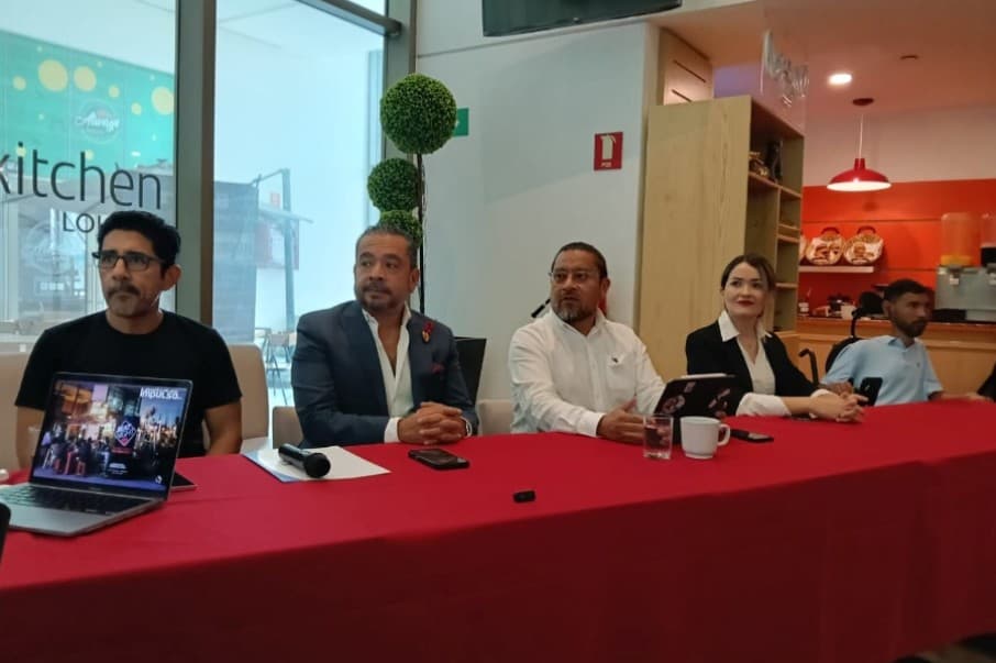 Grupo de empresarios en panel de discusión sentados en mesa con mantel rojo durante evento de negocios en Quintana Roo.