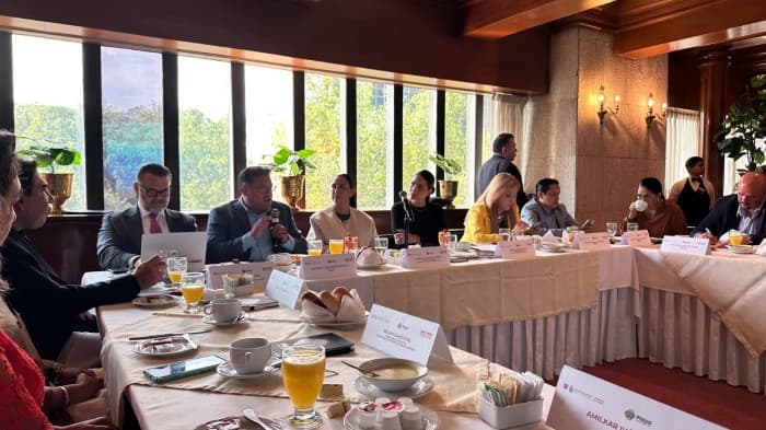 Reunión de negocios en sala de conferencias con autoridades y empresarios alrededor de mesa durante evento de promoción turística.