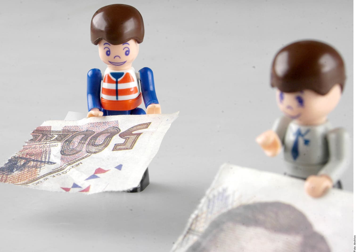 Dos figuras de juguete junto a un billete de euro, una sonriendo y otra de perfil, representando una transacción o intercambio de dinero.