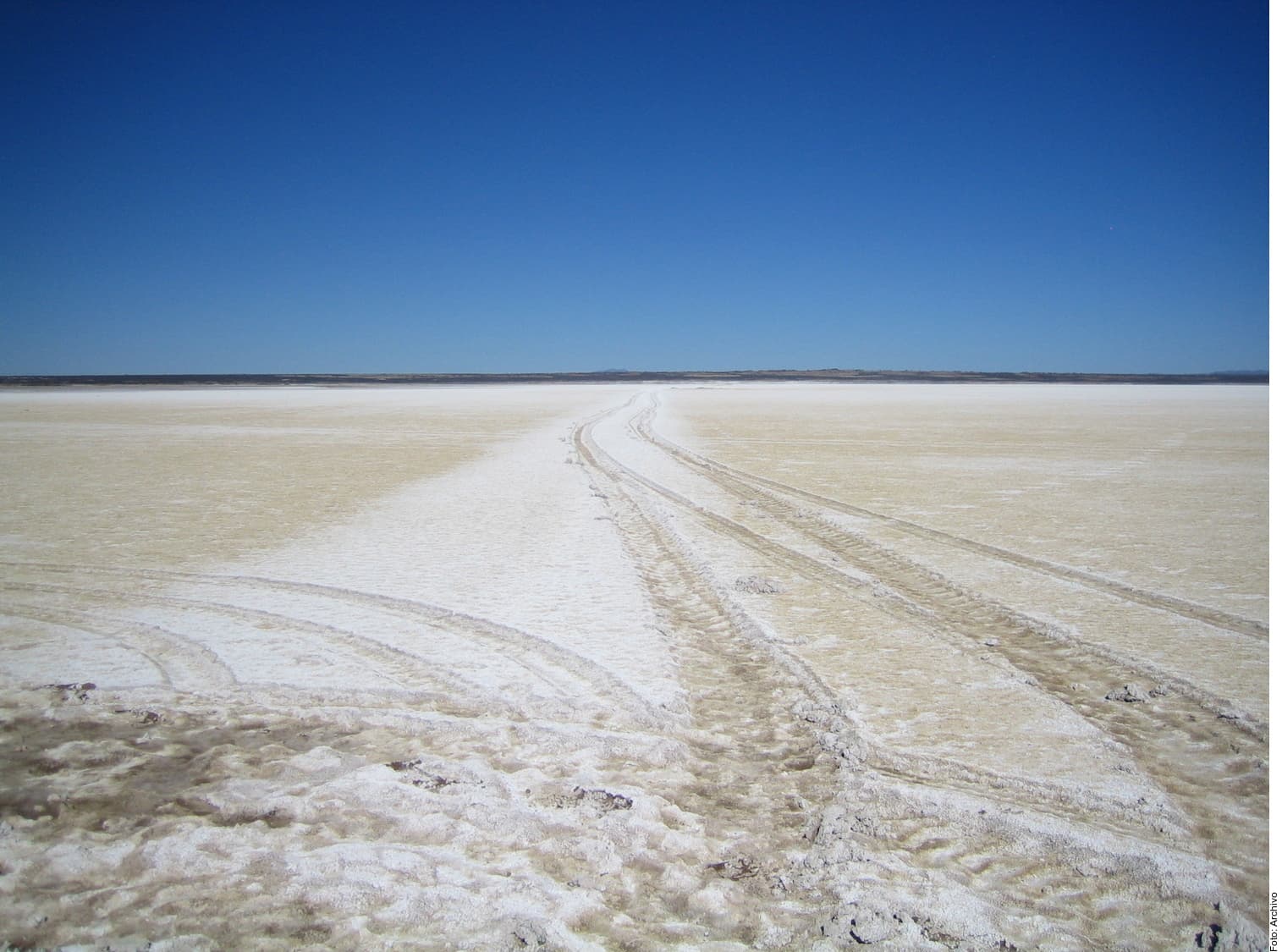 Vía de extracción de litio que cruza un salar desértico de tonalidades blancas y beige bajo cielo azul despejado.