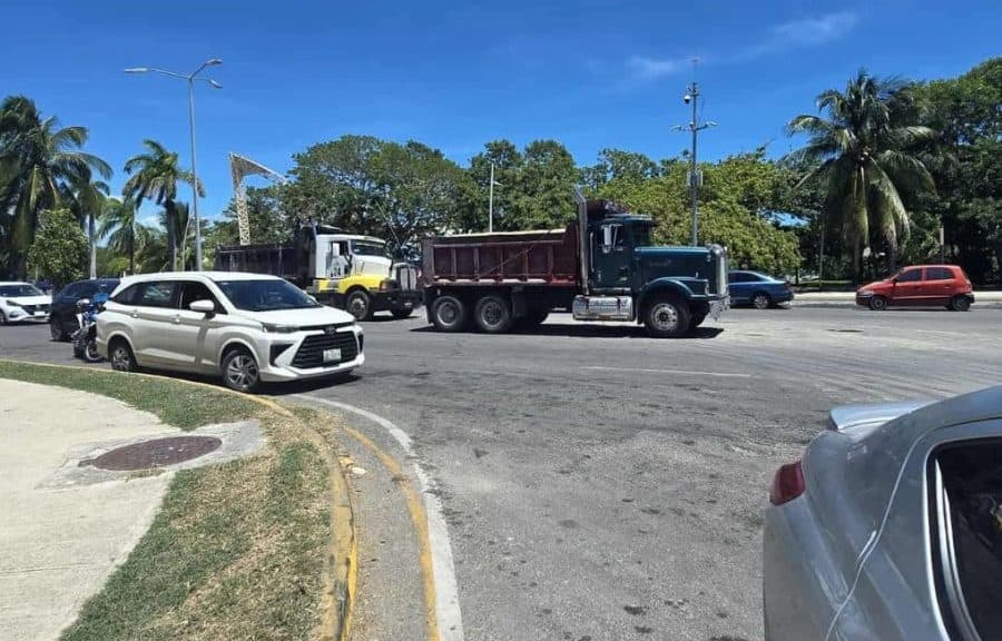 Camiones de volteo y vehículos estacionados en una plaza de Chetumal bajo cielo despejado.
