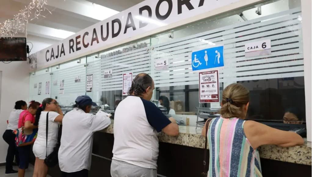 Personas en fila esperan atención en ventanillas de una caja de recaudación municipal con señalización de cajas numeradas.