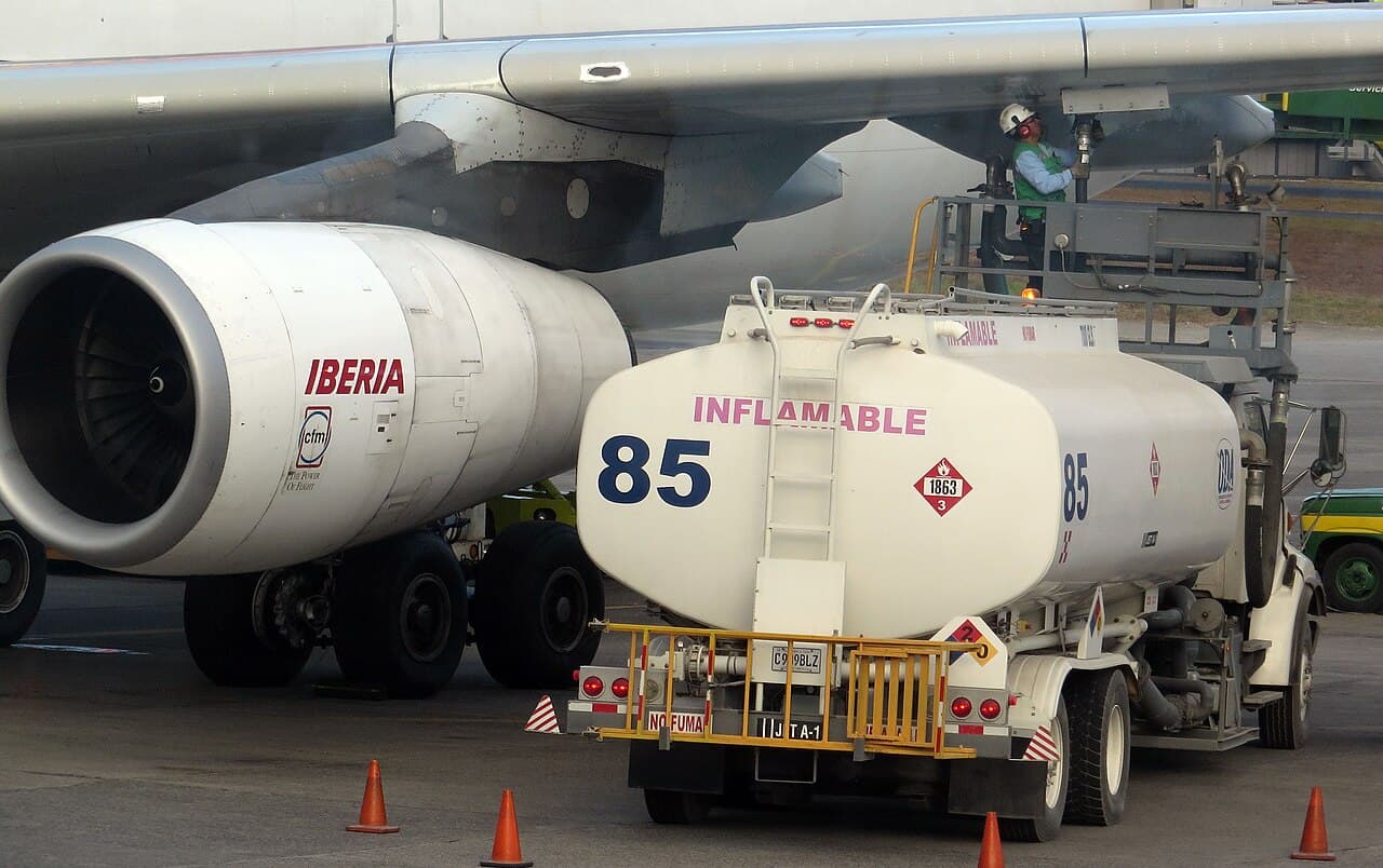 Camión cisterna de combustible INFLAMABLE número 85 siendo cargado junto a un avión Iberia en una terminal aeroportuaria.