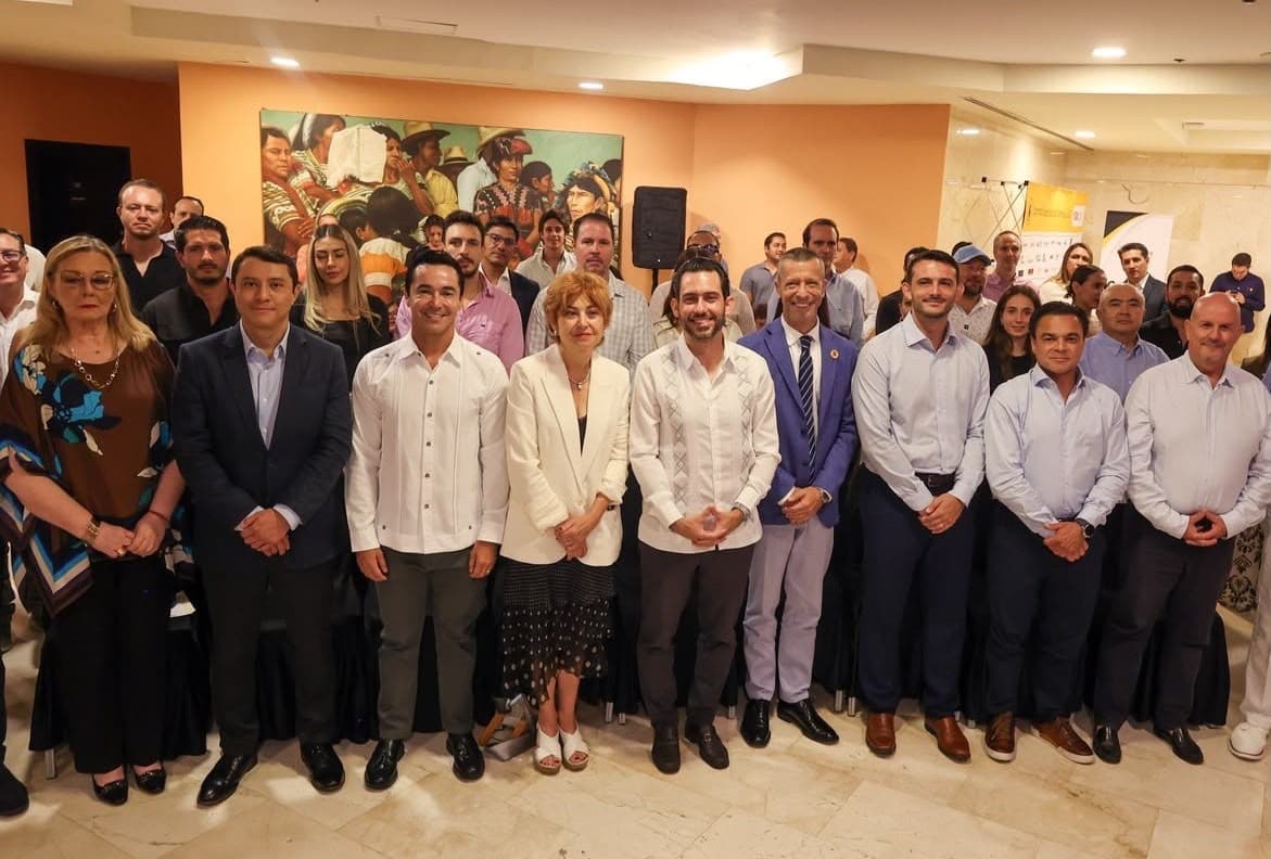 Grupo de personas en traje formal posando para fotografía en una sala con paredes naranjas durante un acto institucional.