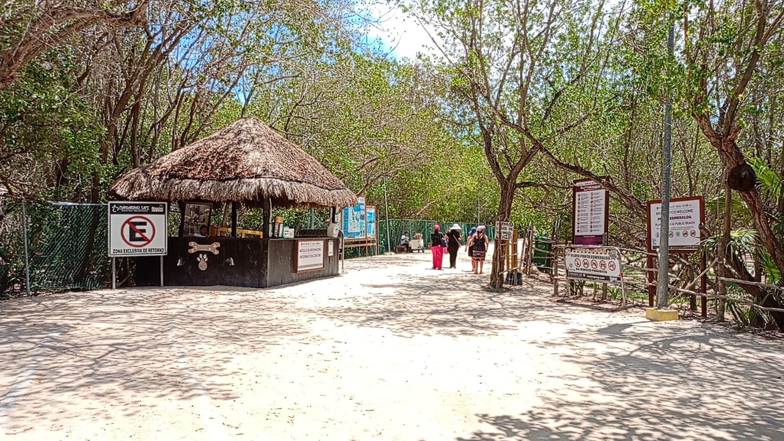 Entrada a Punta Esmeralda con señalización, camino de arena rodeado de vegetación y maleza, con visitantes al fondo