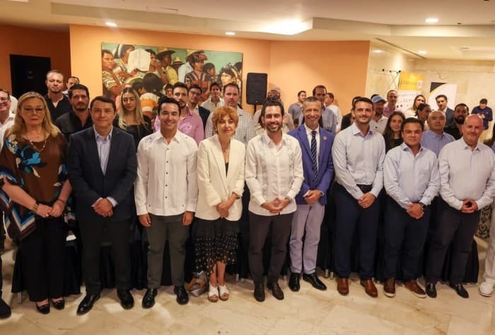 Grupo de personas posando formalmente en línea durante un evento institucional en salón con paredes naranjas.