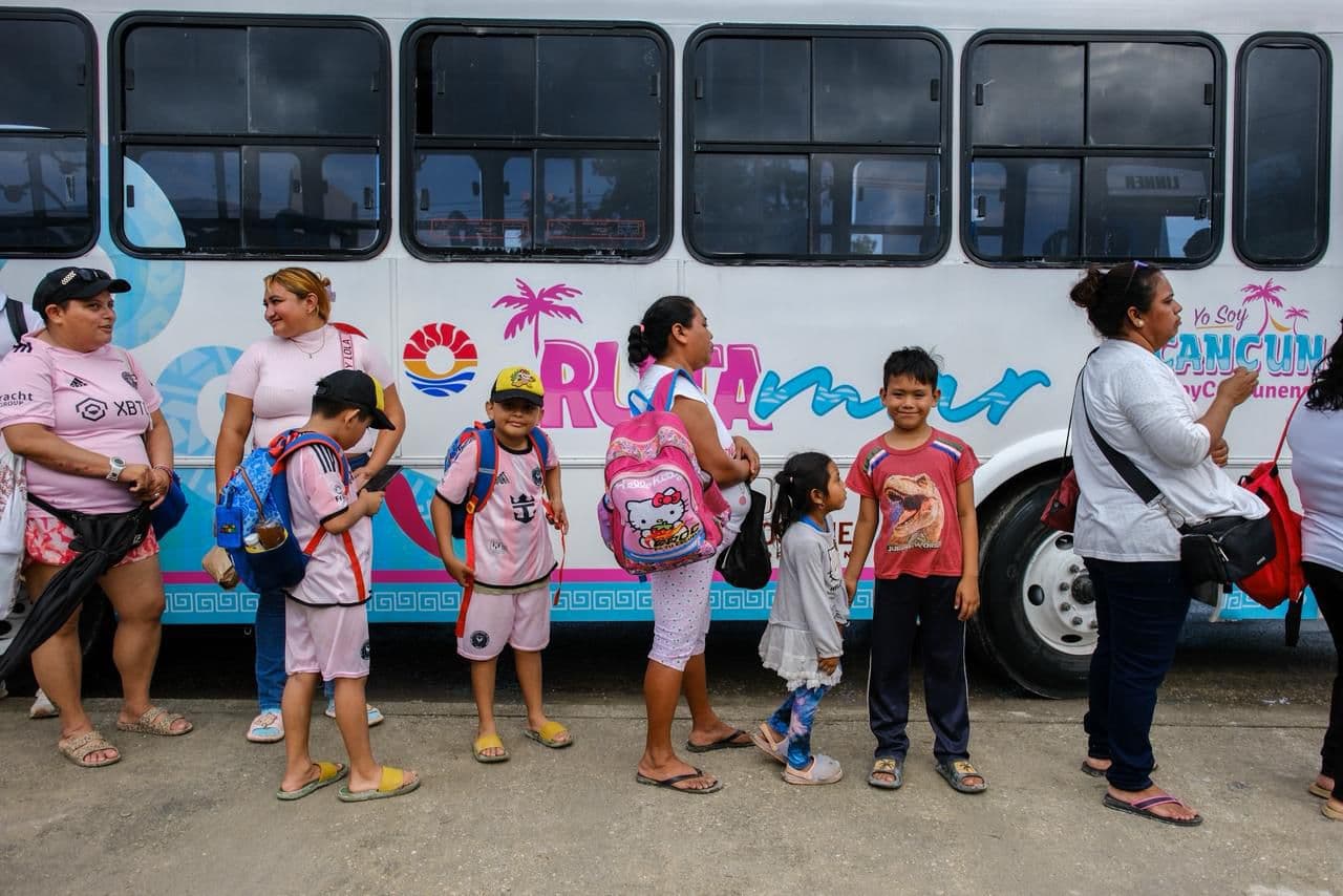 Grupo de adultos y niños de pie frente a un autobús blanco y rosa de Ruta Mar en Cancún.