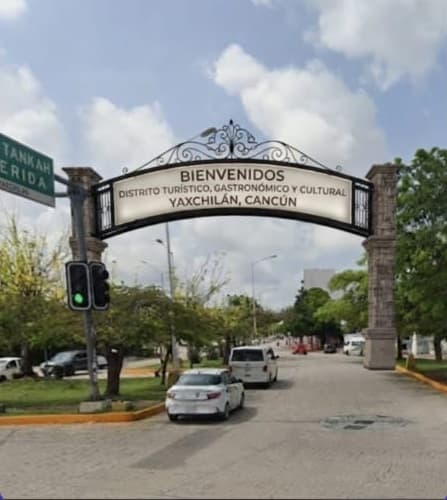 Arco de bienvenida al Distrito Turístico, Gastronómico y Cultural Yaxchilán en Cancún, con avenida, vehículos y vegetación.