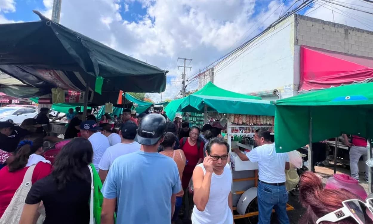Aglomeración de personas en un tianguis con carpas verdes y negras, algunos vendedores y compradores en un mercado sobre ruedas.