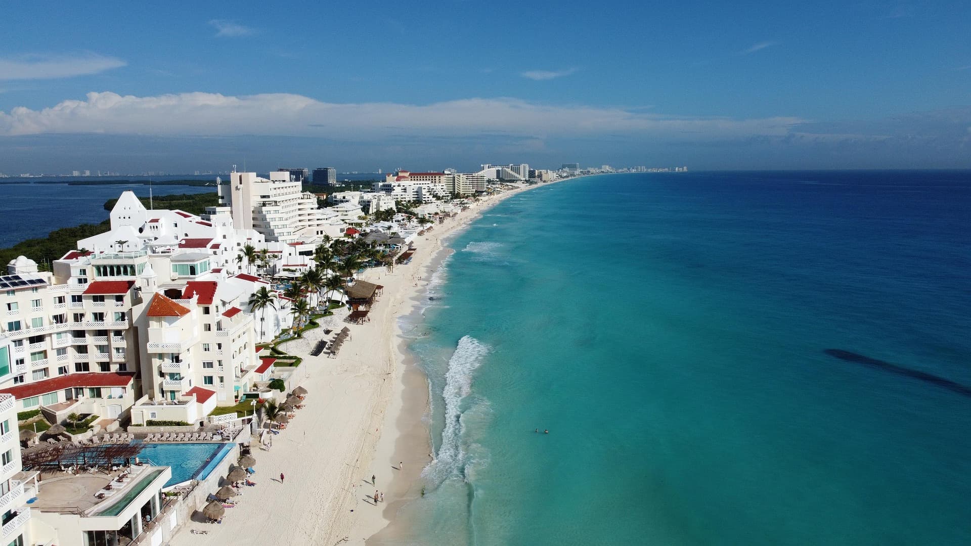 Vista aérea de la zona hotelera de Cancún con playas turquesas, edificios de hospedaje y resort frente al mar Caribe.