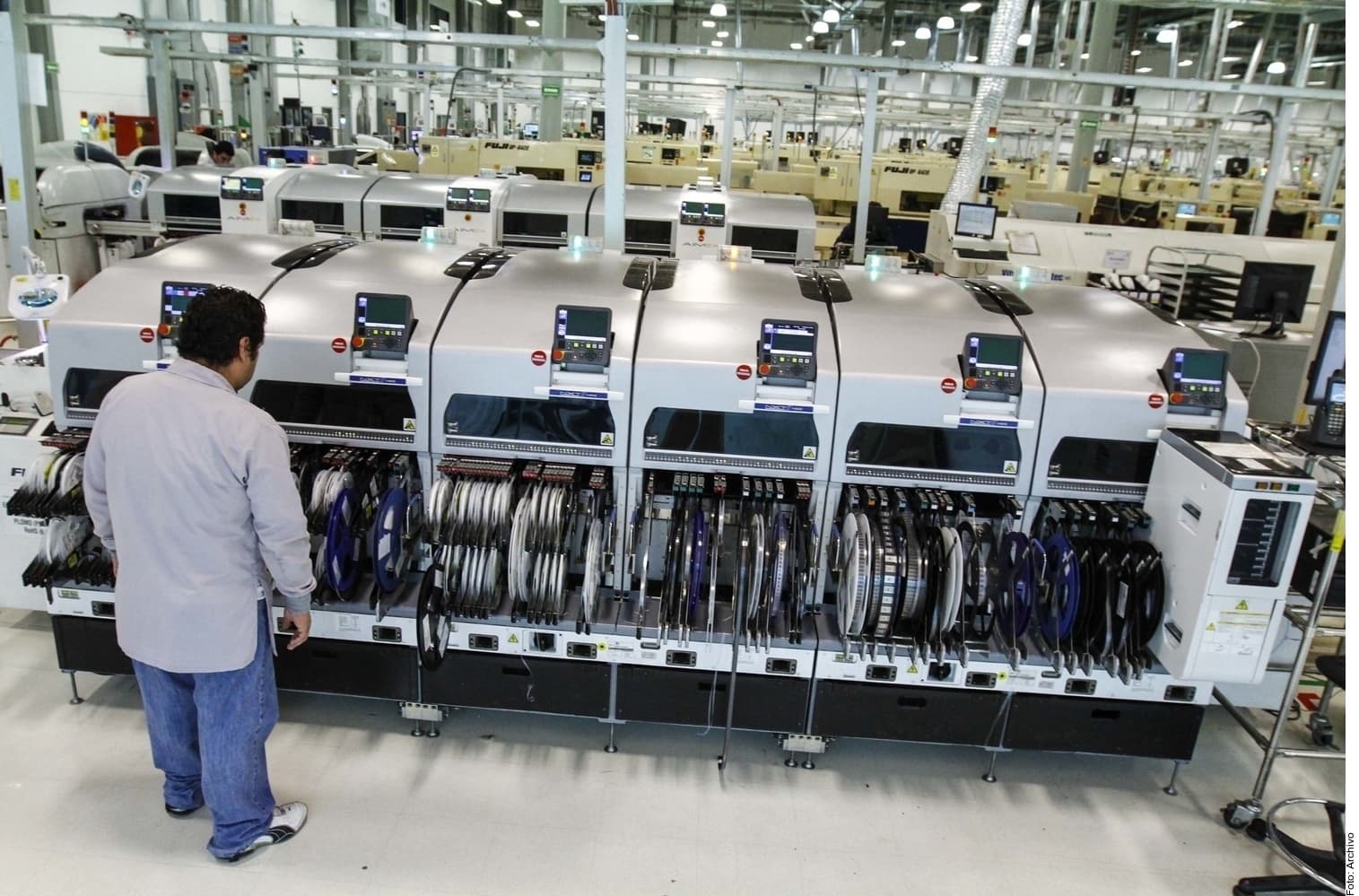 Operario supervisa máquinas de manufactura de componentes electrónicos en planta industrial.