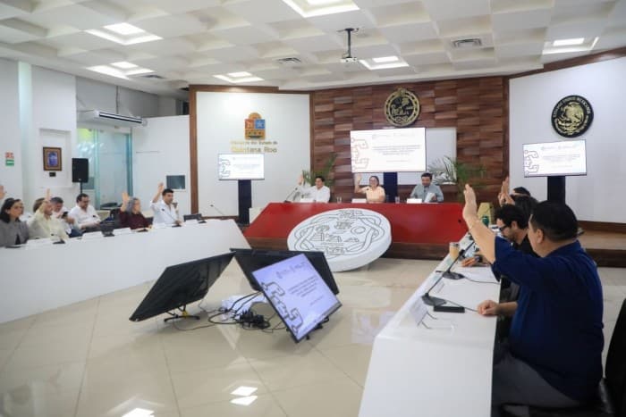 Sesión del Cabildo de Playa del Carmen con funcionarios y ciudadanos en sala de sesiones con mesa directiva y pantallas de presentación.