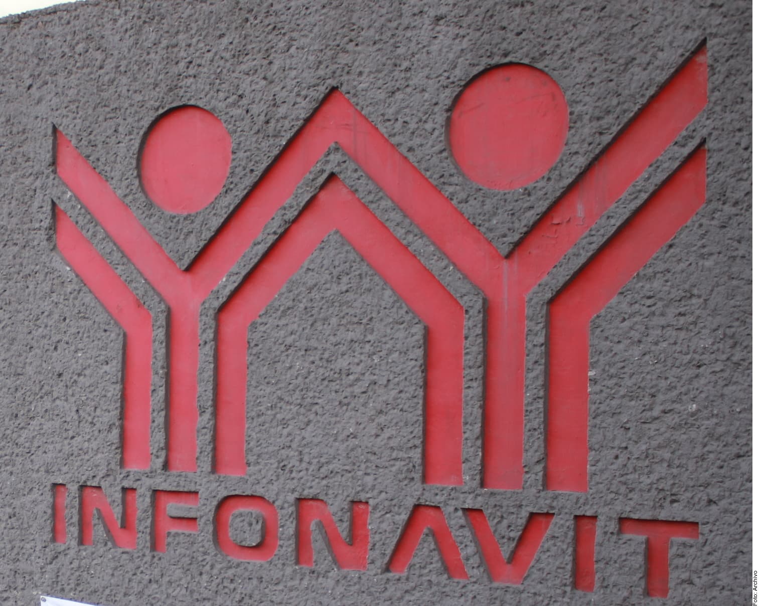 Logo del Infonavit en relieve rojo sobre pared gris de concreto.