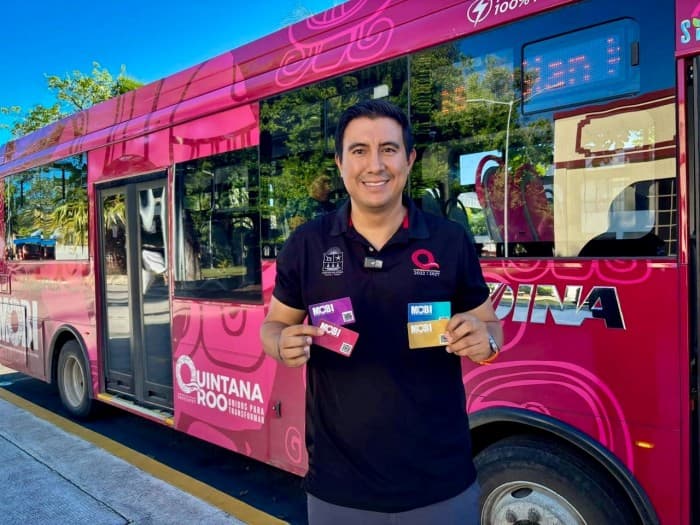 Persona sostiene tarjetas de pago electrónico frente a un autobús rosa del sistema MOBI en Chetumal.