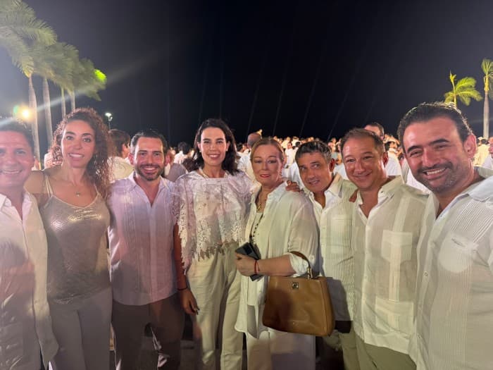 Grupo de personas en atuendo formal blanco en un evento nocturno con palmeras de fondo en ambiente tropical.
