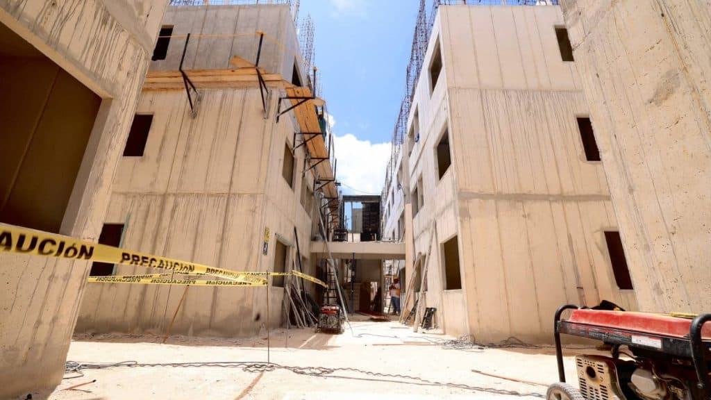 Obra en construcción con edificios de concreto en fase de estructura, cinta de precaución amarilla y equipo de trabajo en el sitio.
