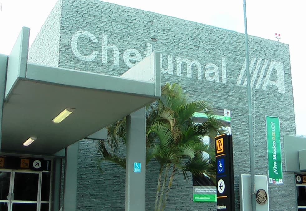 Fachada frontal del Aeropuerto Internacional de Chetumal con señalización de accesibilidad y vegetación tropical.