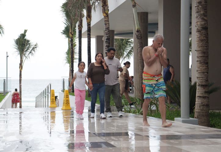 Grupo de turistas disfruta del área común de un resort frente al mar en Quintana Roo, con palmeras y arquitectura moderna de lujo.