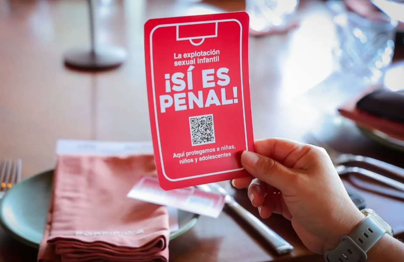 Mano sostiene tarjeta roja con mensaje sobre explotación sexual infantil y código QR, en contexto de campaña de protección.