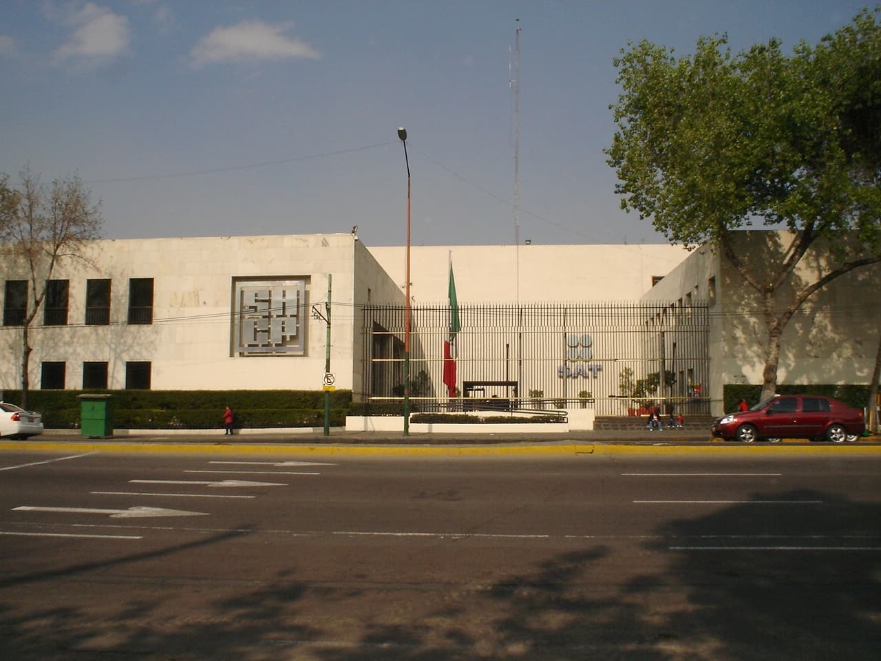 Edificio institucional de arquitectura moderna con fachada blanca, bandera mexicana y acceso controlado.