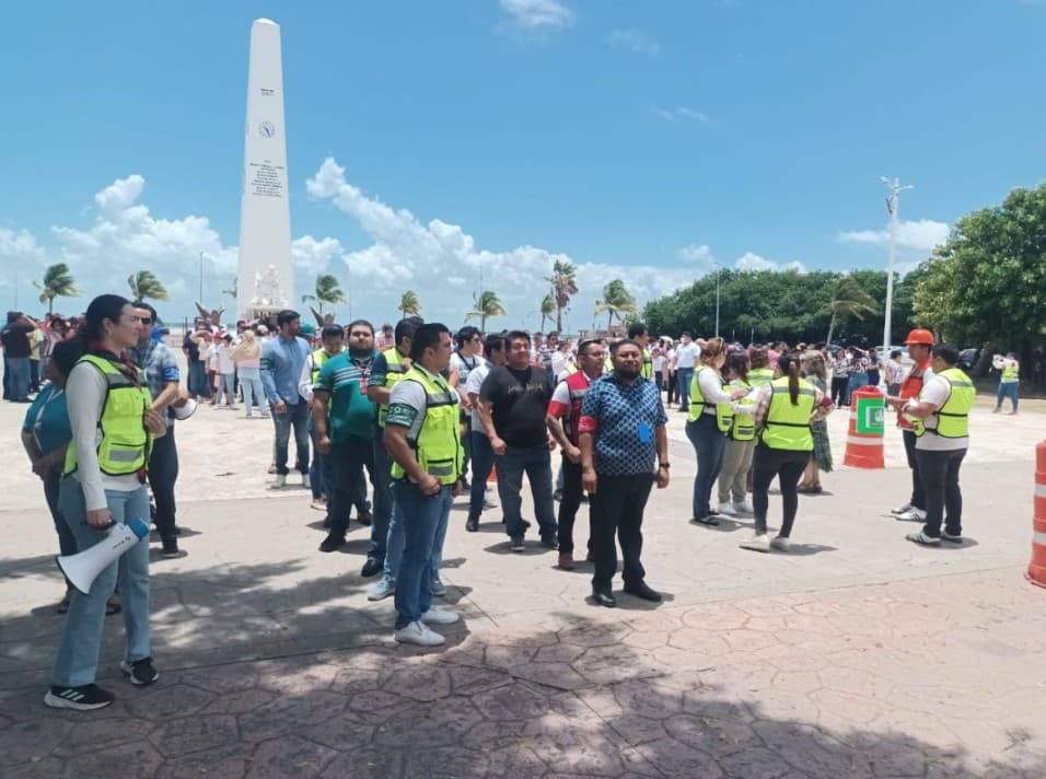 Personal de protección civil y autoridades coordinan a ciudadanos durante un simulacro de emergencia frente a un monumento, bajo cielo despejado.