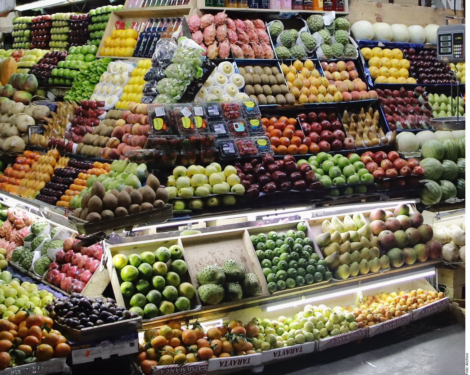 Puesto de venta de frutas y verduras frescas organizadas en cajas y bandejas en un mercado.
