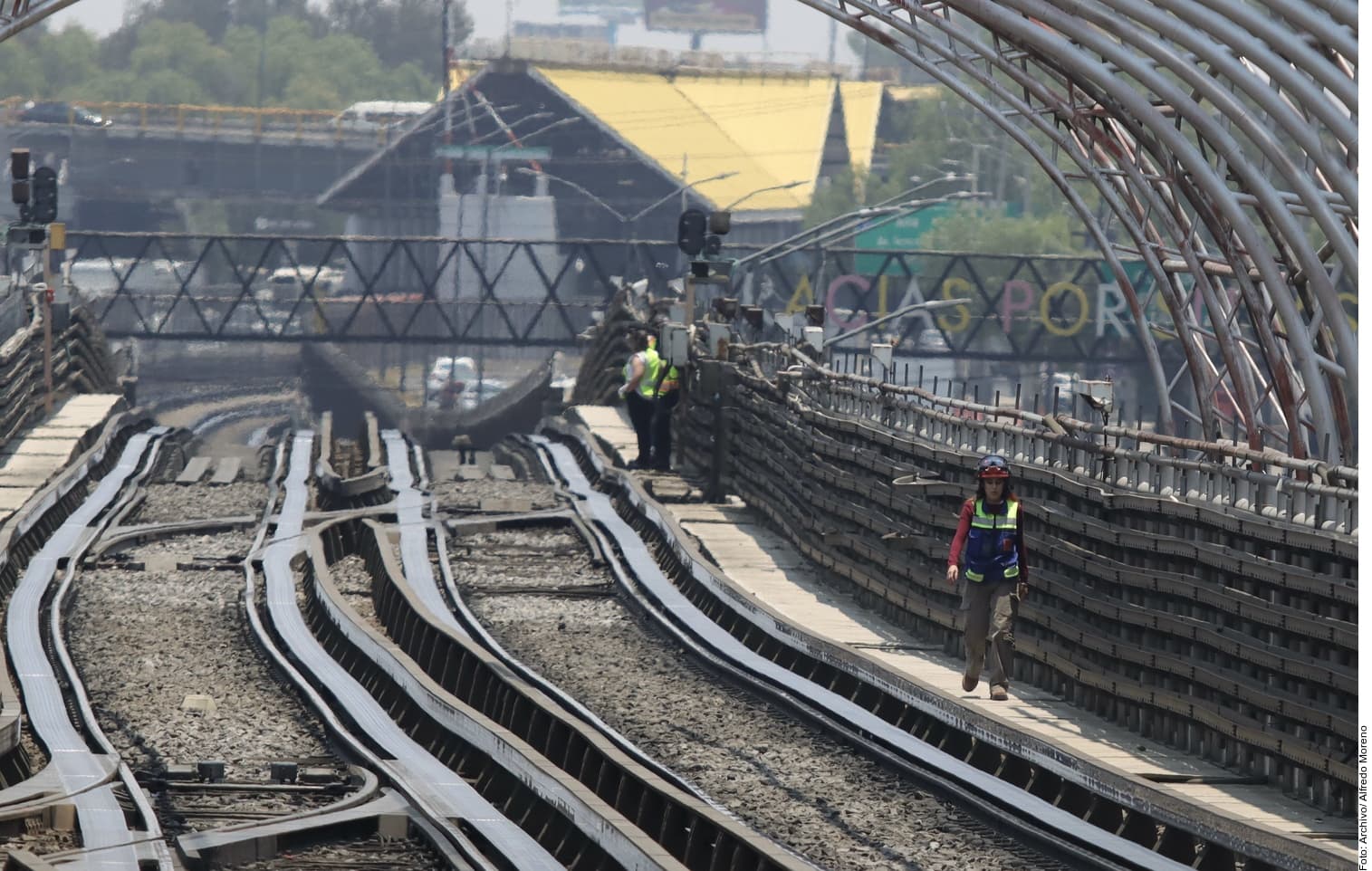 Trabajadores en equipo de seguridad inspeccionan infraestructura ferroviaria en construcción o mantenimiento dentro de una estructura metálica.