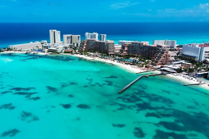 Vista aérea de la zona hotelera de Cancún con playas de arena blanca, aguas turquesas y edificios de hospedaje frente al mar.