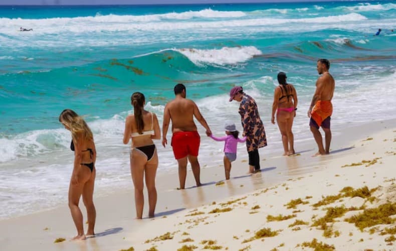 Grupo de turistas en una playa con aguas turquesas y olas, disfrutando de actividades recreativas acuáticas.