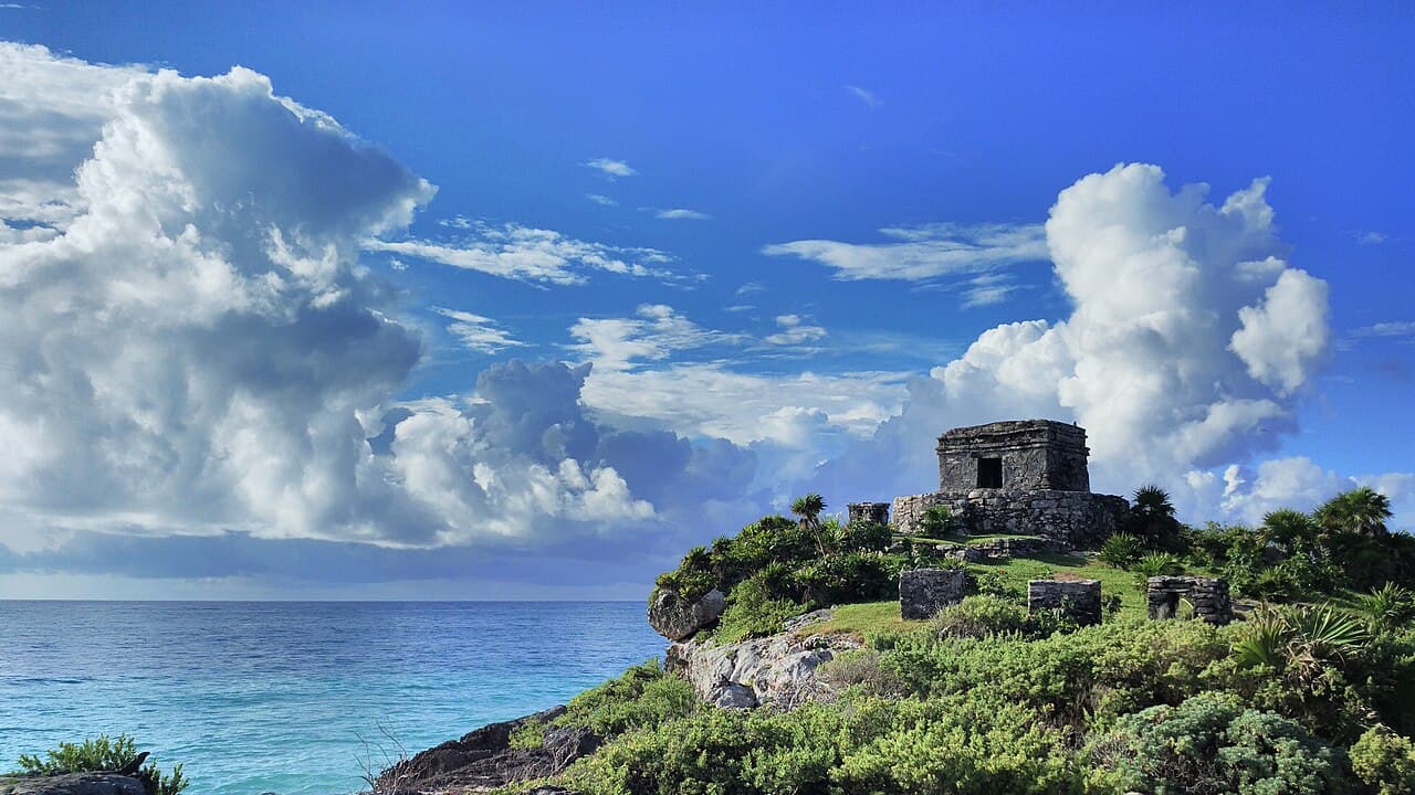 Ruinas mayas en acantilado frente al mar Caribe con vegetación tropical y cielo azul con nubes blancas
