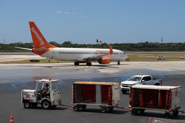 Avión de pasajeros con bandera mexicana en la pista de un aeropuerto, rodeado de vehículos de servicio.