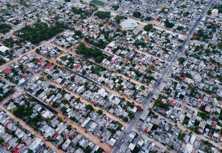 Vista aérea de una zona urbana densamente poblada con viviendas residenciales, calles ordenadas y áreas verdes dispersas.