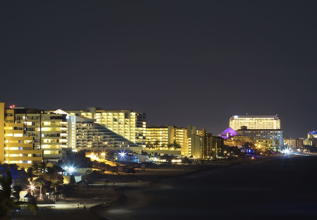 Vista nocturna de hoteles y complejos turísticos iluminados en una playa del Caribe mexicano.