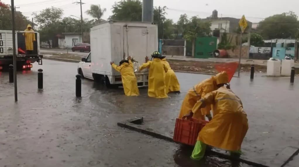 Personal municipal con equipos de protección amarillos trabaja en calles inundadas durante operativo de respuesta a lluvias intensas en Cancún.