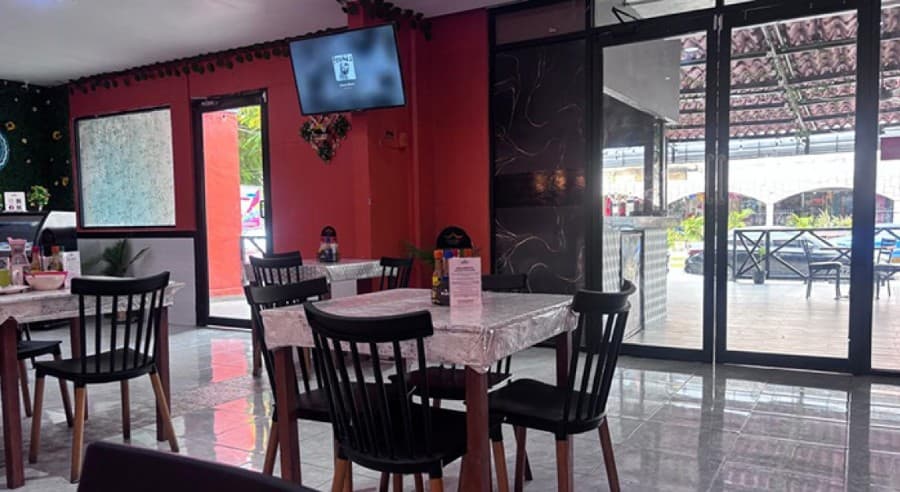 Interior de restaurante vacío con mesas, sillas negras y puertas de acceso a terraza, mostrando espacio comercial sin clientes.