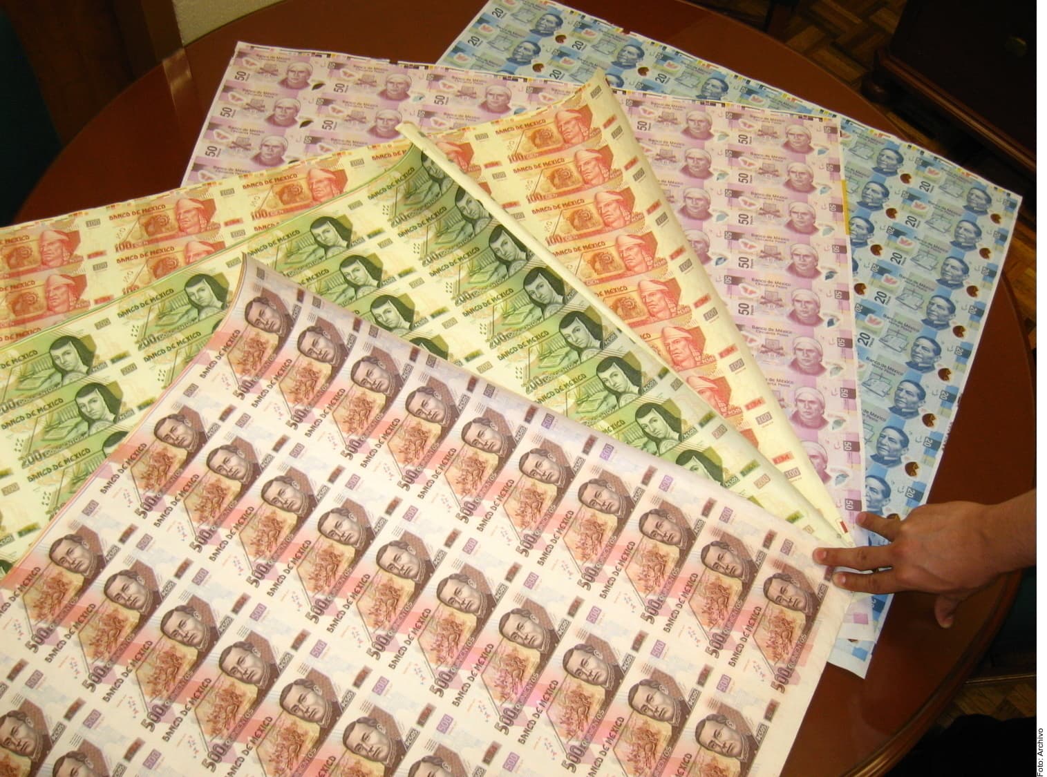 Hojas de billetes mexicanos de diferentes denominaciones (50, 100 y 20 pesos) dispuestas sobre una mesa de madera.