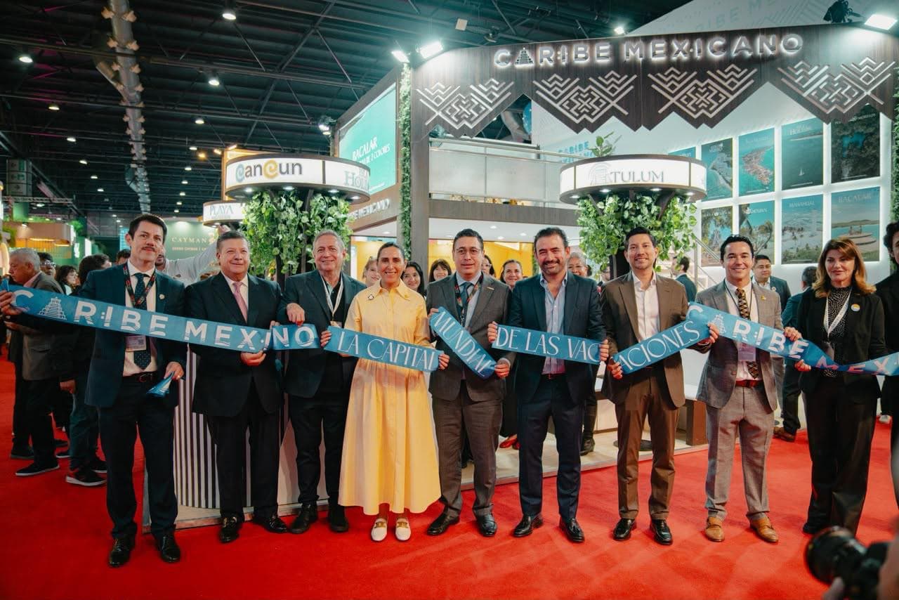 Funcionarios y autoridades de turismo sostienen una cinta azul durante la inauguración del stand de Caribe Mexicano en una feria de turismo internacional.