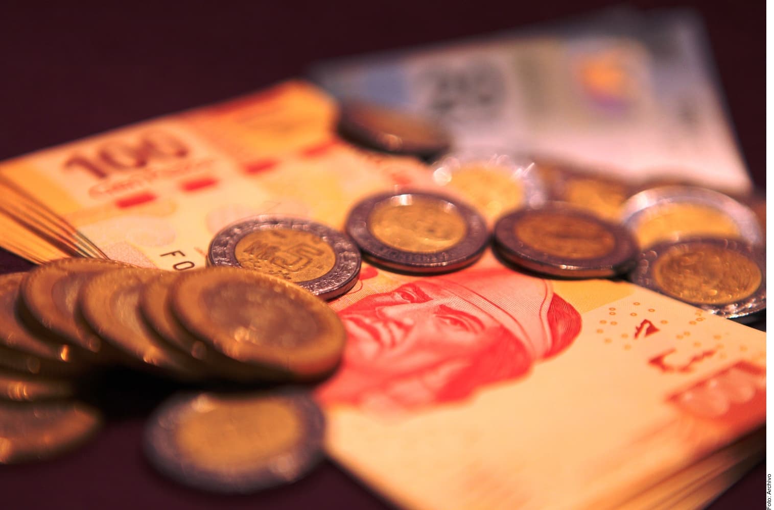 Billetes y monedas de pesos mexicanos sobre una superficie oscura, con enfoque en las monedas en primer plano.