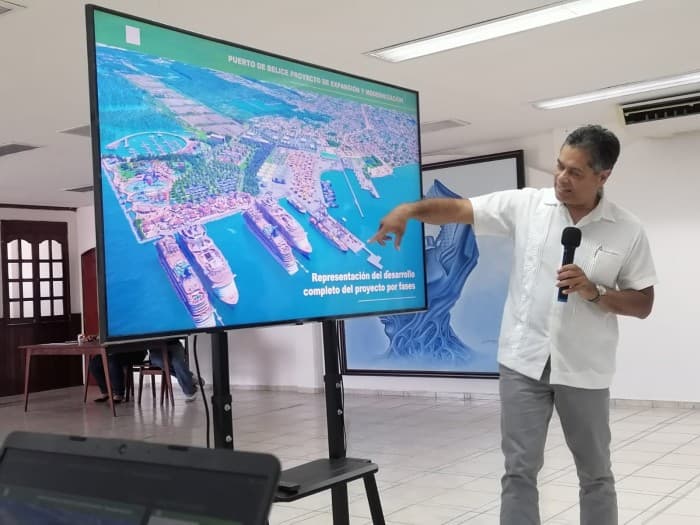 Presentador señala un mapa aéreo de un proyecto portuario durante una exposición en una sala de conferencias.