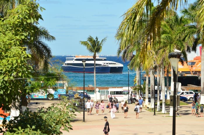 Ferry de pasajeros atracado en terminal portuaria de Cozumel con turistas en la zona de embarque y palmeras tropicales.