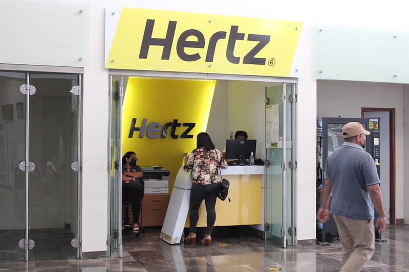 Cliente en mostrador de arrendadora Hertz en terminal de aeropuerto o centro comercial.
