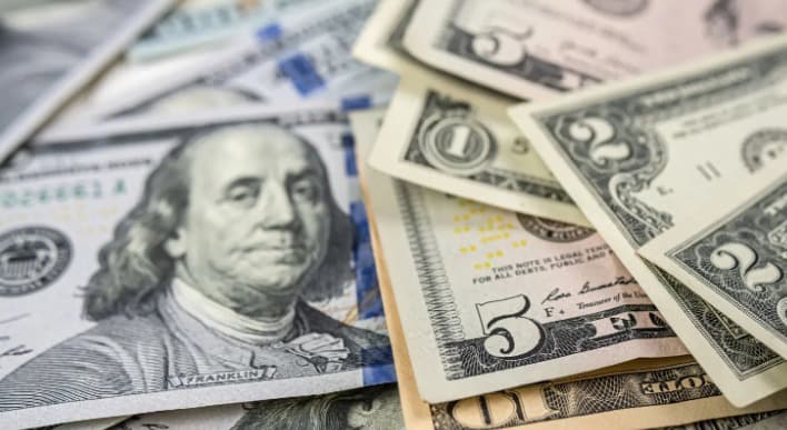 Billetes de dólar estadounidense y mexicano superpuestos, mostrando denominaciones de 100 y 5 dólares con moneda mexicana de fondo.