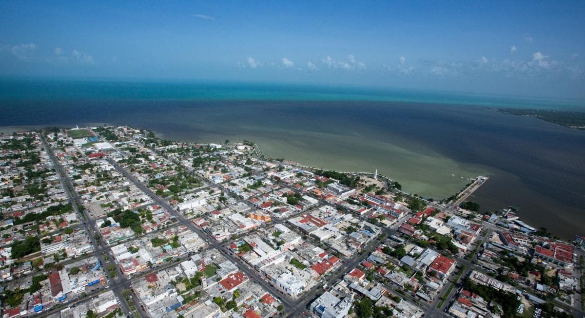 Vista aérea de Chetumal mostrando la zona urbana, infraestructura vial y la bahía con agua turquesa al fondo.