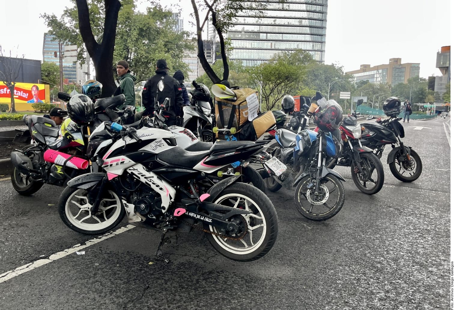 Grupo de trabajadores en motocicletas y motos taxi estacionadas en una avenida urbana durante una concentración o manifestación.