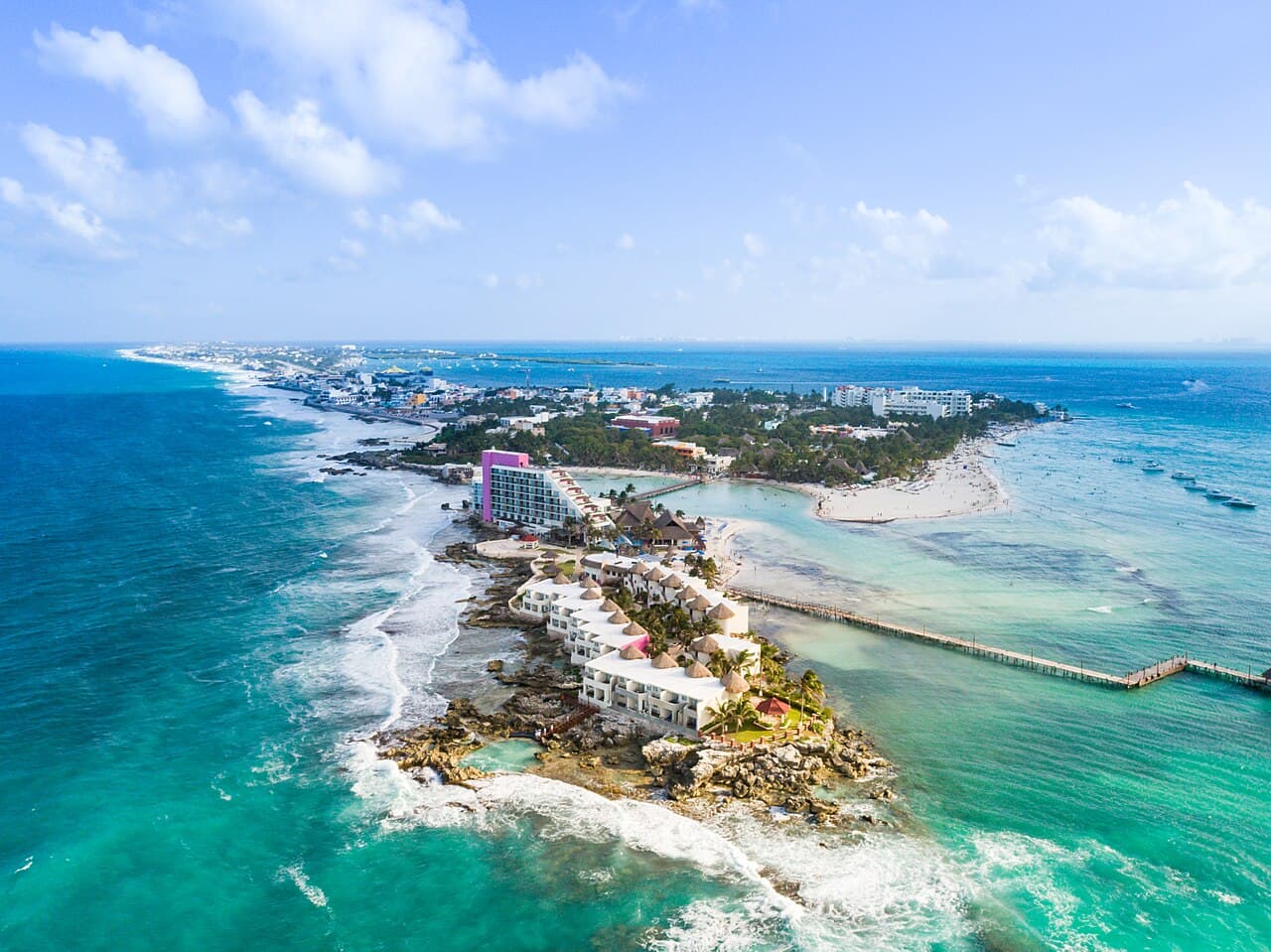 Vista aérea de un resort hotelero en una península rocosa de Quintana Roo, México, con playas de arena blanca, aguas turquesas y embarcaciones en la bahía.