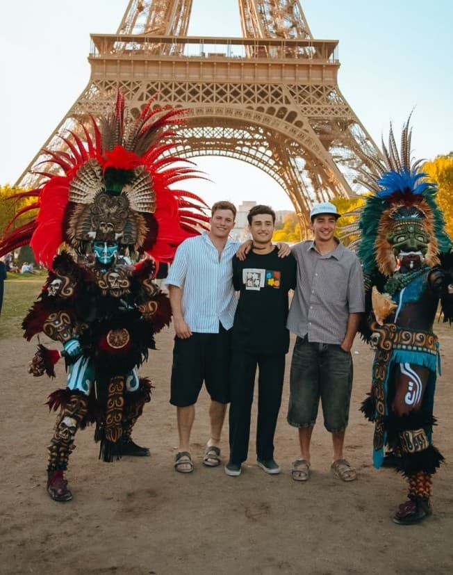 Tres turistas posan con dos personajes disfrazados de figuras prehispánicas frente a la Torre Eiffel en París.
